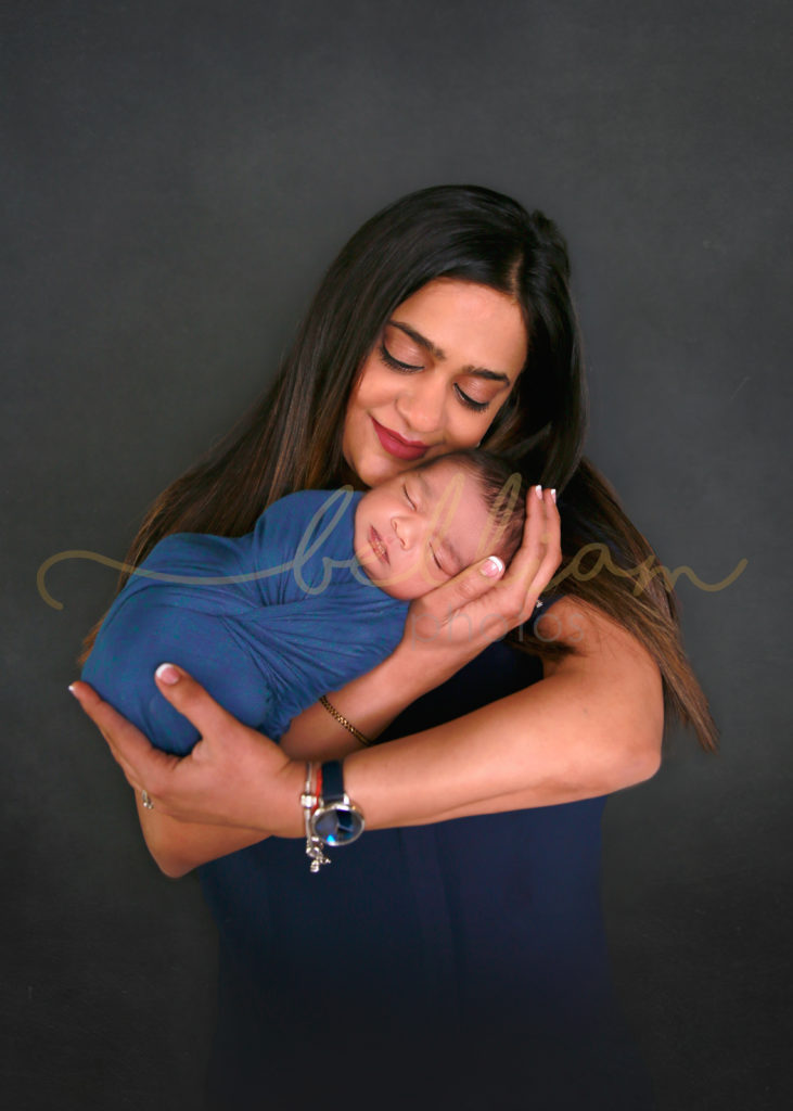alt="newborn baby boy wrapped in a blue wrap being held by mom"