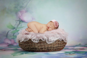 alt="newborn baby girl bum up pose on a basket with floral background"