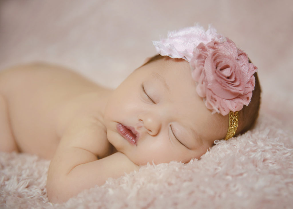alt="calgary newborn pictures baby girl on a pink furry blanket with pink and gold headband"