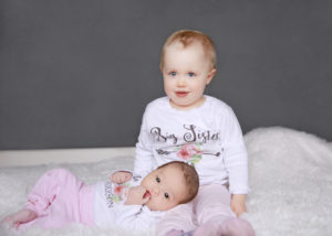 alt="newborn baby girl and big sister smiling at the camera"