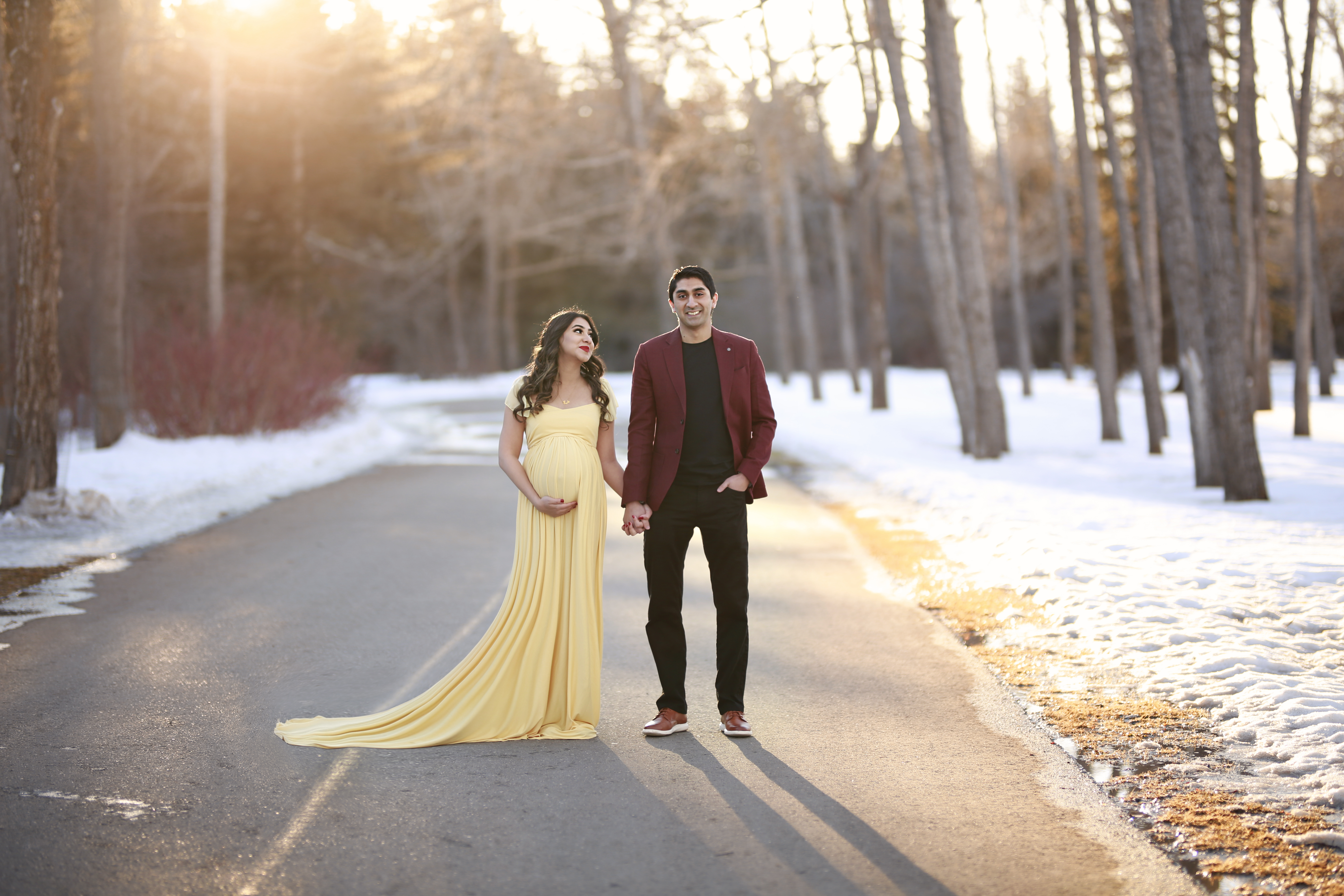 alt="beautiful mother to be in a yellow maternity gown standing with her husband at sunset"
