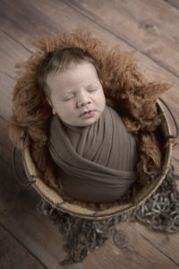 newborn baby boy in a brown wrap in a backet