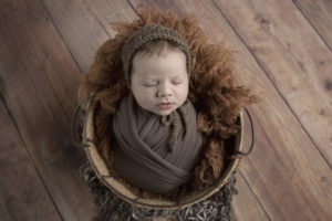 newborn baby boy in a brown wrap in a basket