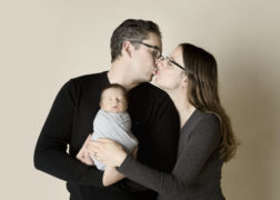 couple kissing while holding a newborn