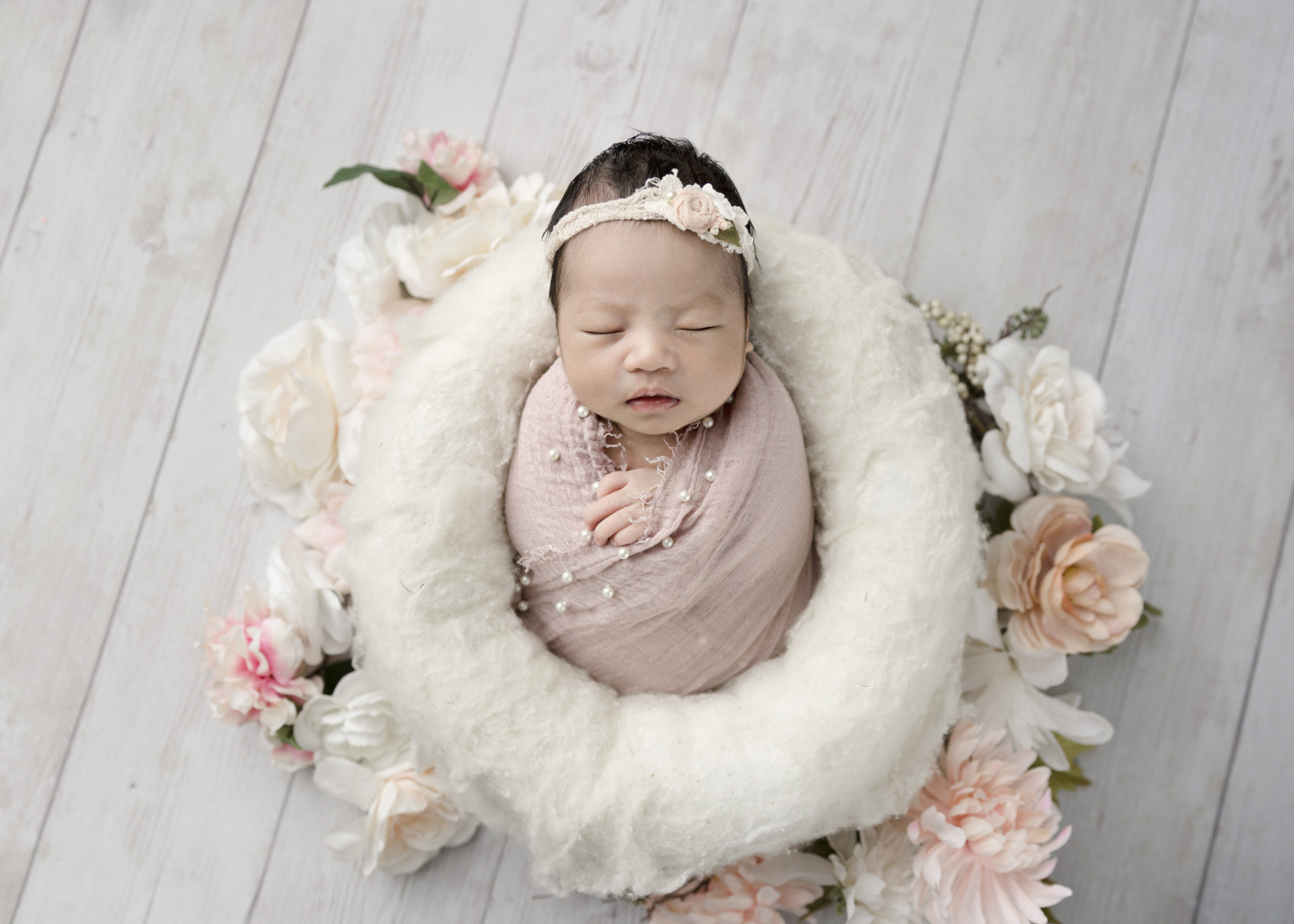 newborn baby girl in a pink wrap surrounded by flowers
