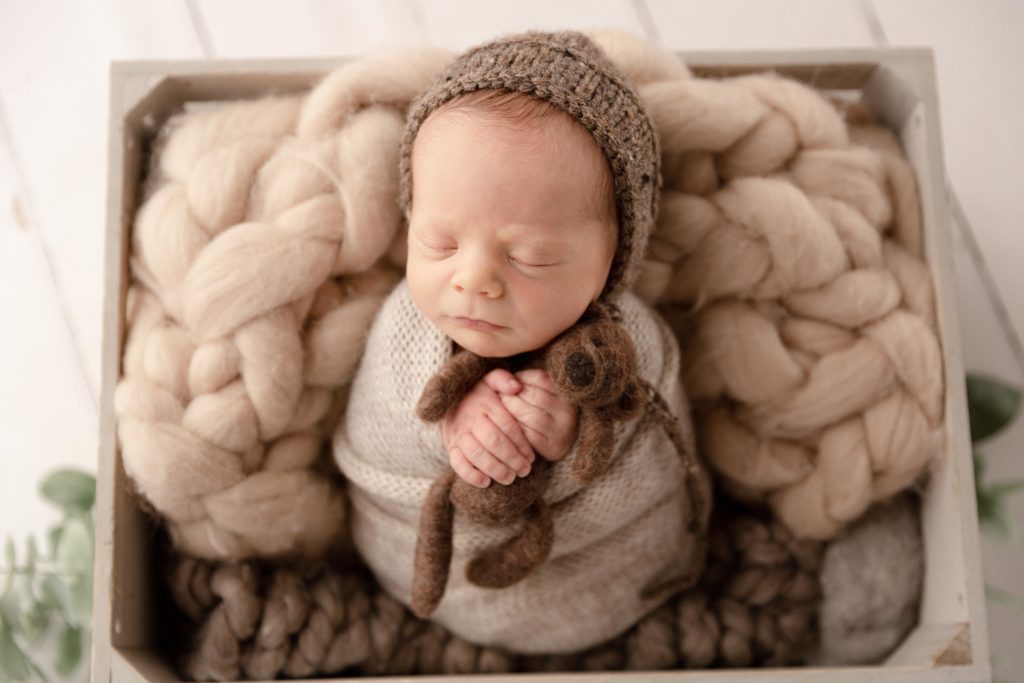 newborn baby boy in a prop holding a brown teddy bear