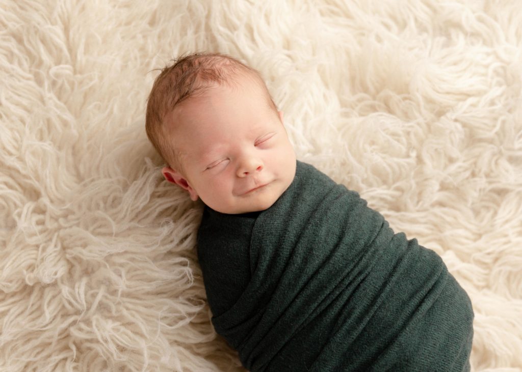 newborn baby boy in green wrap smiling