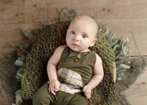 3 month old baby in a green onsie on a green blanket wrapped in a bl Calgary baby photographer Belliam Photos
