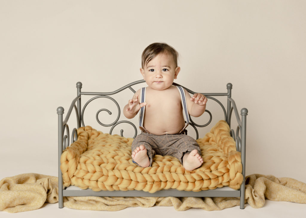 Baby boy one year old on a baby bed with a yellow knit blanket