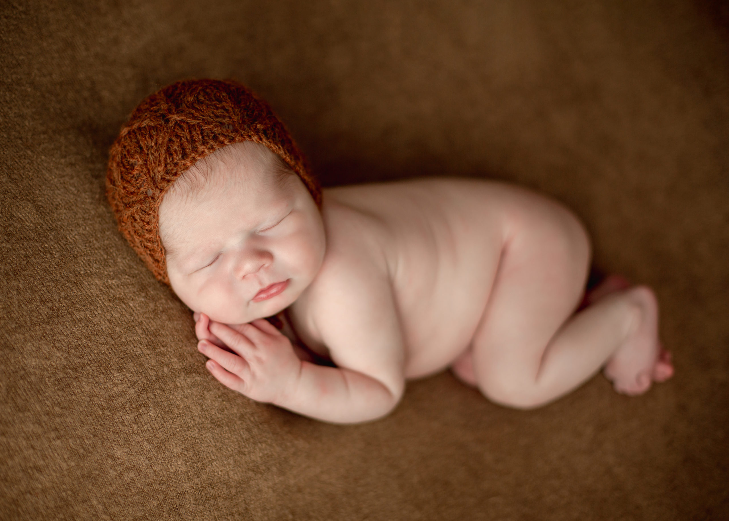 Newborn baby in a burnt orange knit hat