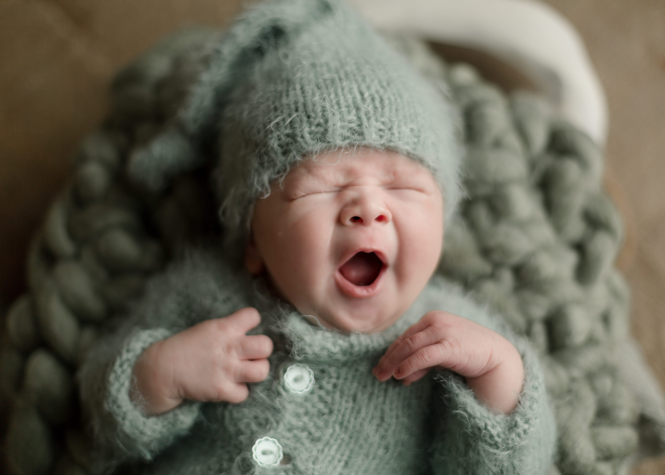 yawning newborn in a green knit outfit