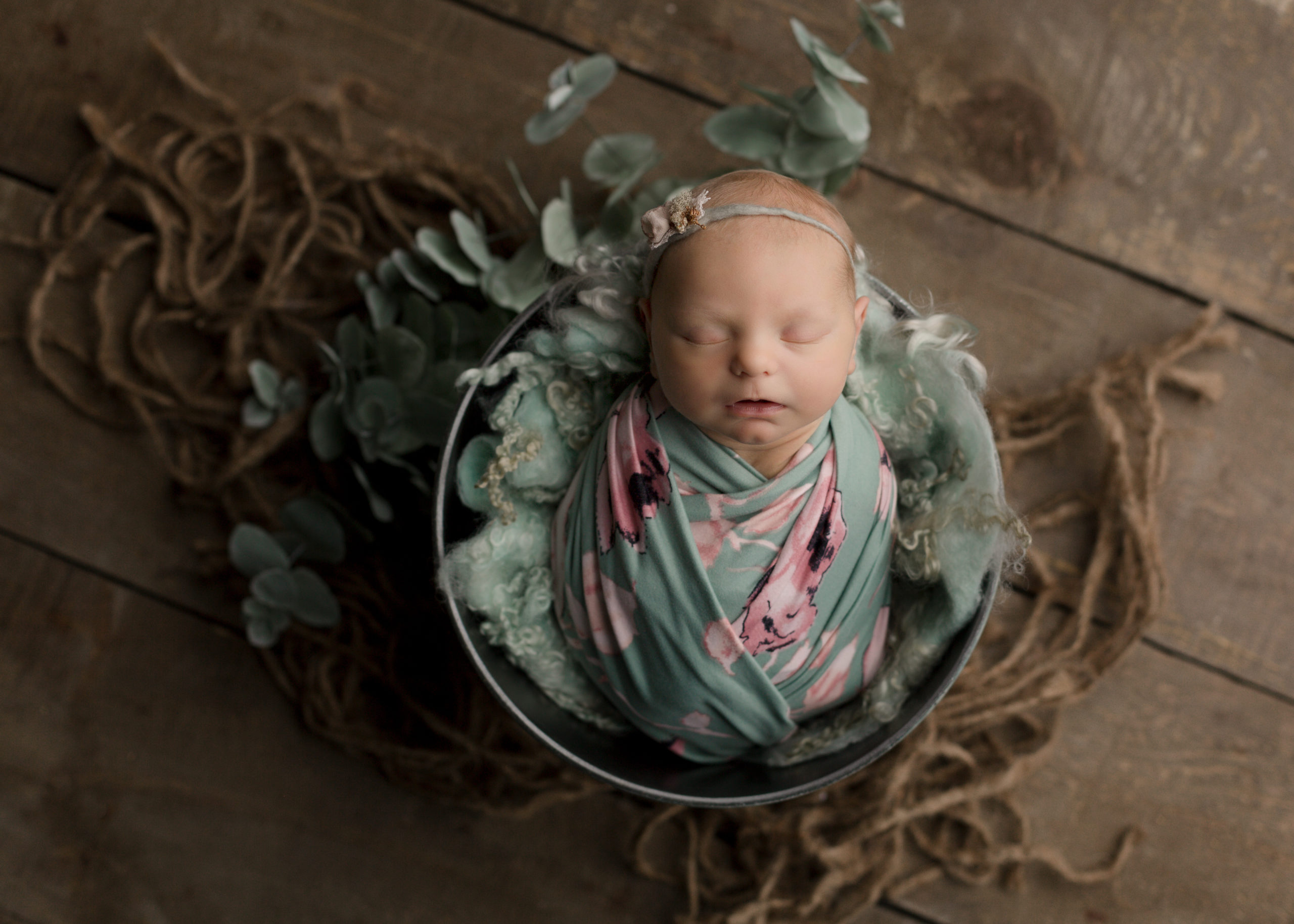 Baby in green floral wrap in a bucket