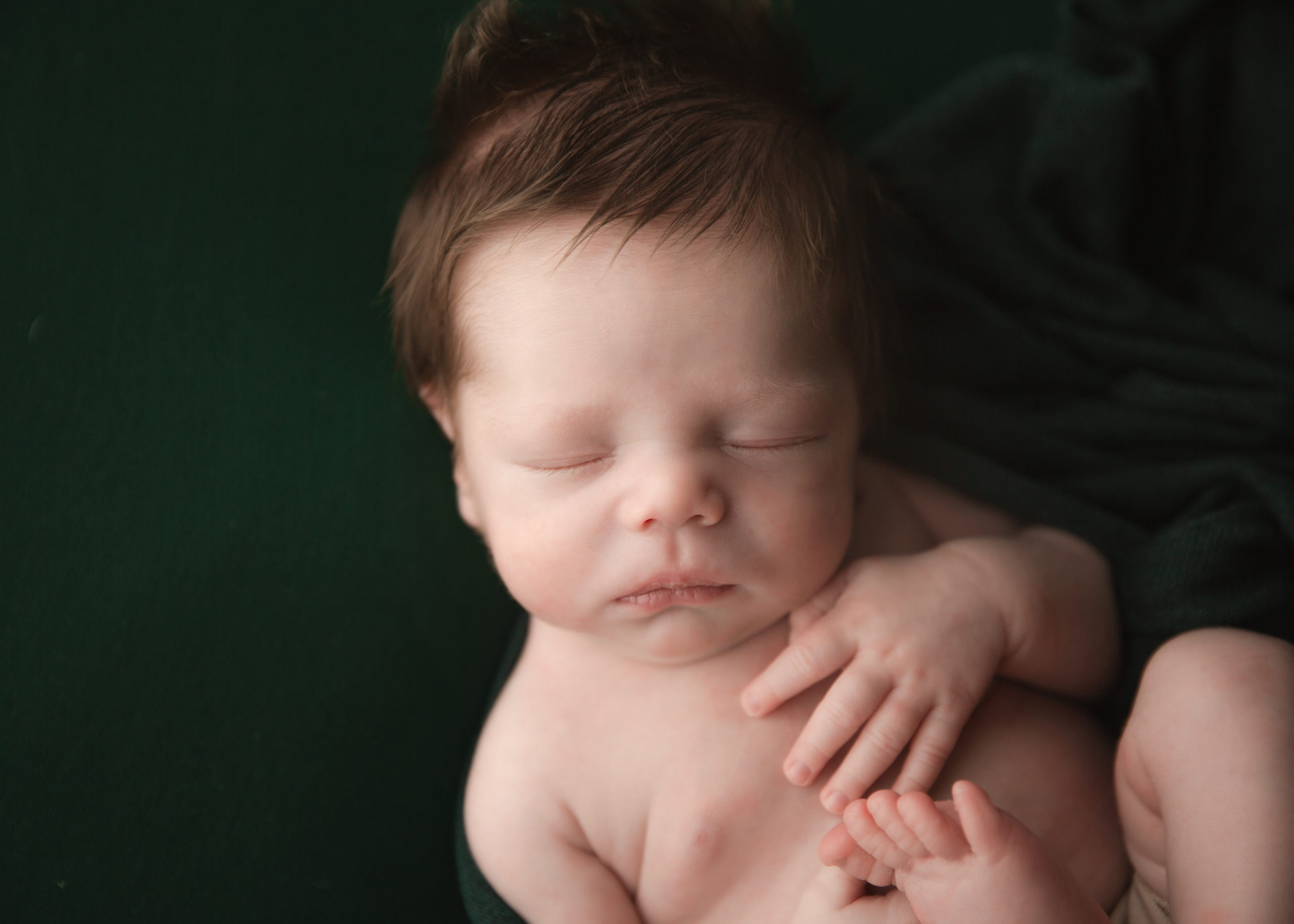 Newborn baby boy on a dark green blanket sleeping