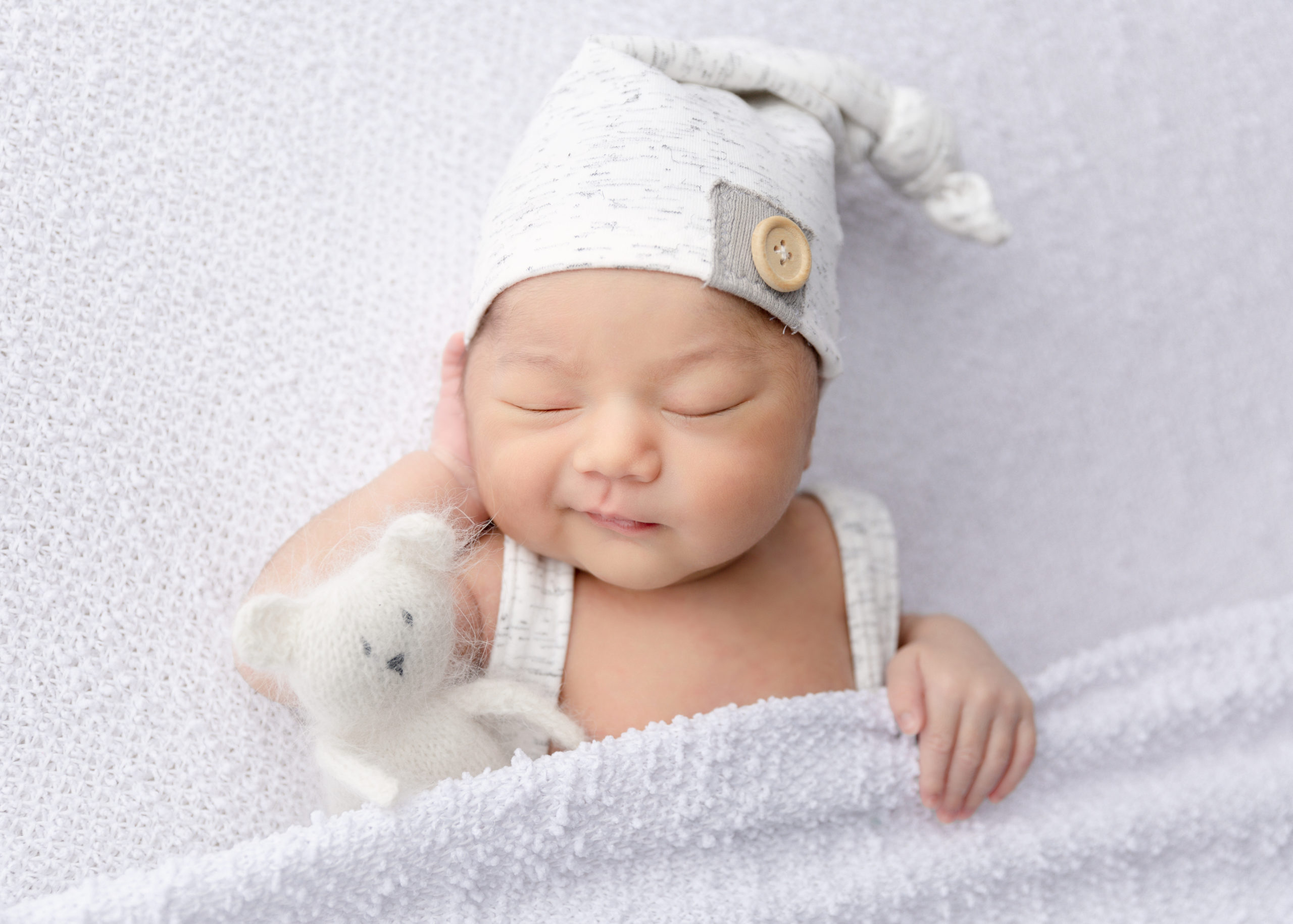 Newborn baby boy in grey smirking with a white bear stuffy