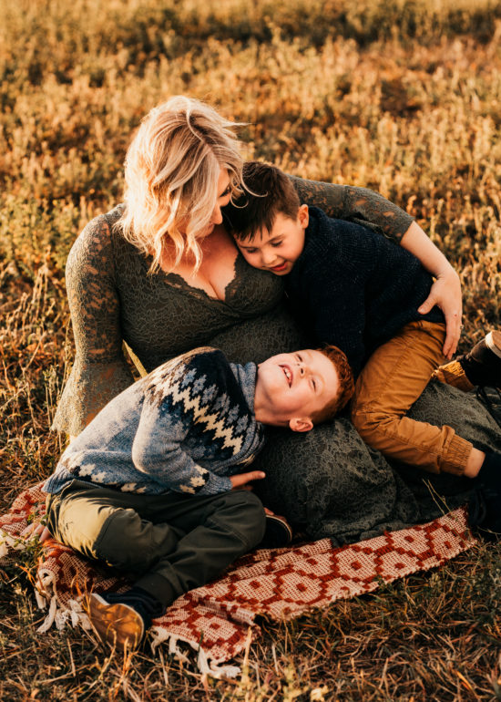 Mom and her two boys sitting on a blanket in a field cuddling