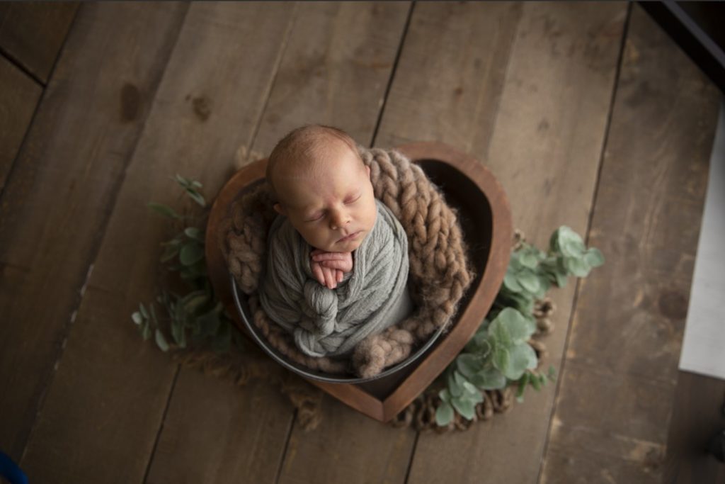 Baby boy in a green wrap in a bucket posed for a newborn photoshoot