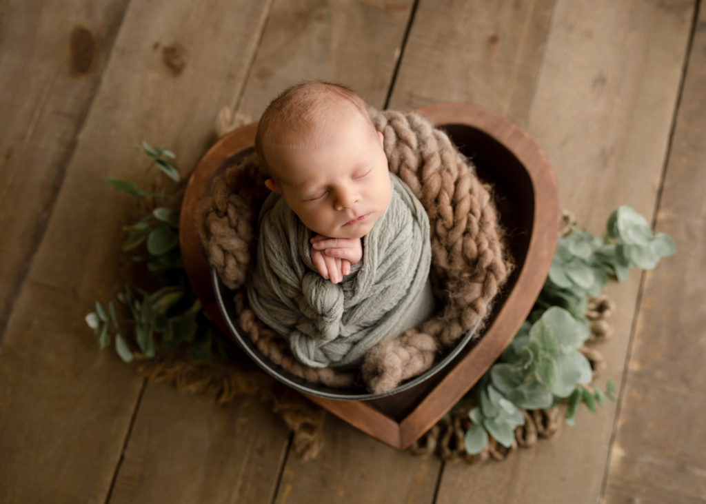 Baby boy in a green wrap in a bucket posed for a newborn photoshoot