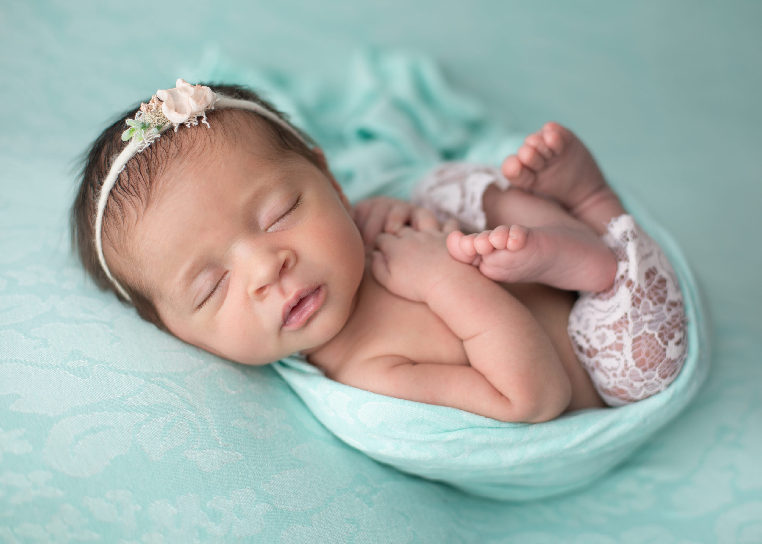 Newborn baby wrapped in a teal blanket on a teal floral blanket