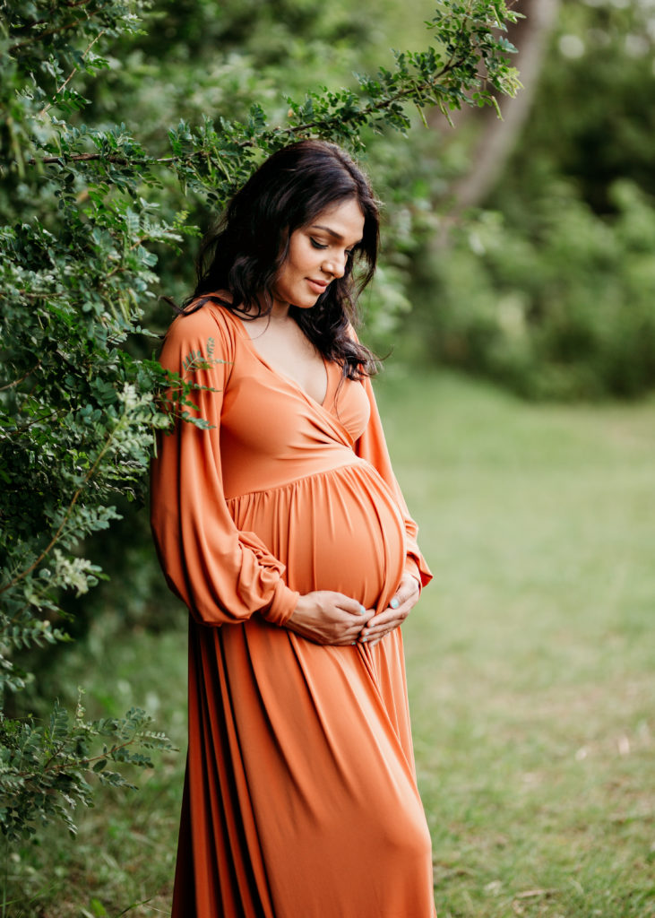 Pregnant woman looking at her belly in orange gown - Calgary Prenatal Massage
