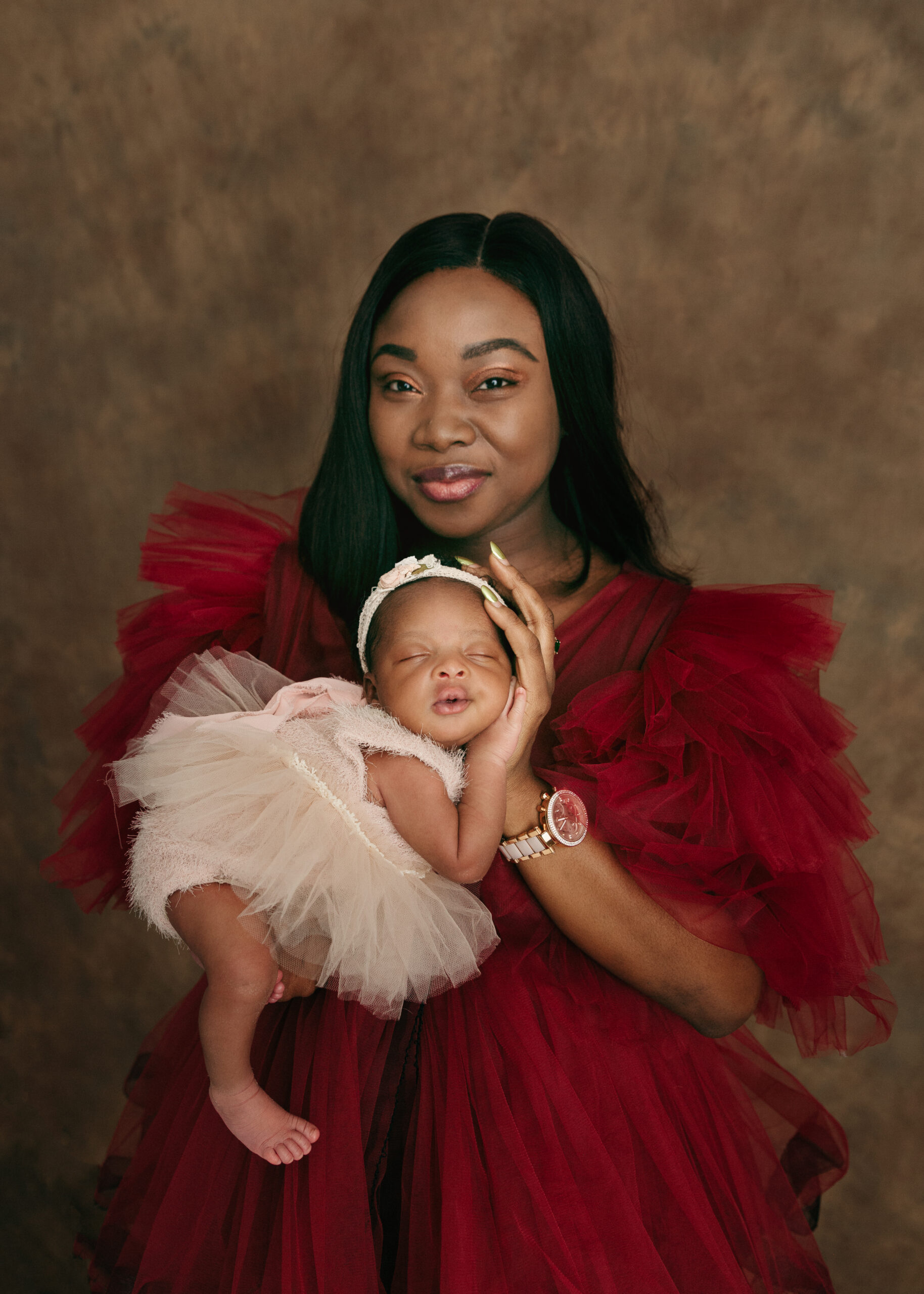 Mom holding her newborn baby in a red gown baby in a pink dress